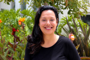 Alicia Mignano, smiling while wearing a black shirt, sits in front of flowers planted at the Pico branch of the Santa Monica Public Library system.